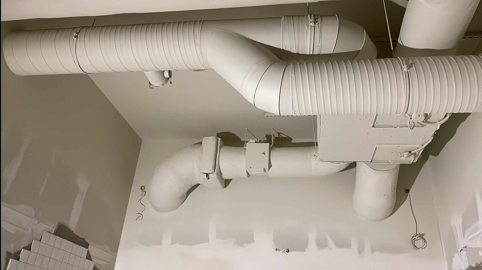 Białe, pomalowane rury wentylacyjne pod sufitem w trakcie wykańczania wnętrza. Widoczne łączenia i elementy mocujące. Ściany przygotowane do malowania.