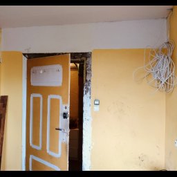 USŁUGI U RAFAŁA Rafał Zieliński - Żółta ściana w trakcie remontu z wiszącymi kablami, częściowo otwarte drzwi z pomalowanymi fragmentami i widocznymi śladami prac remontowych.