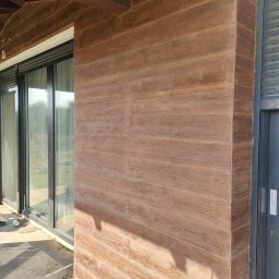 USŁUGI U RAFAŁA Rafał Zieliński - Elewacja budynku w Gniezno z drewnopodobną okładziną, widoczne przesuwne okna i fragment drzwi. Detal wykończenia zewnętrznego.