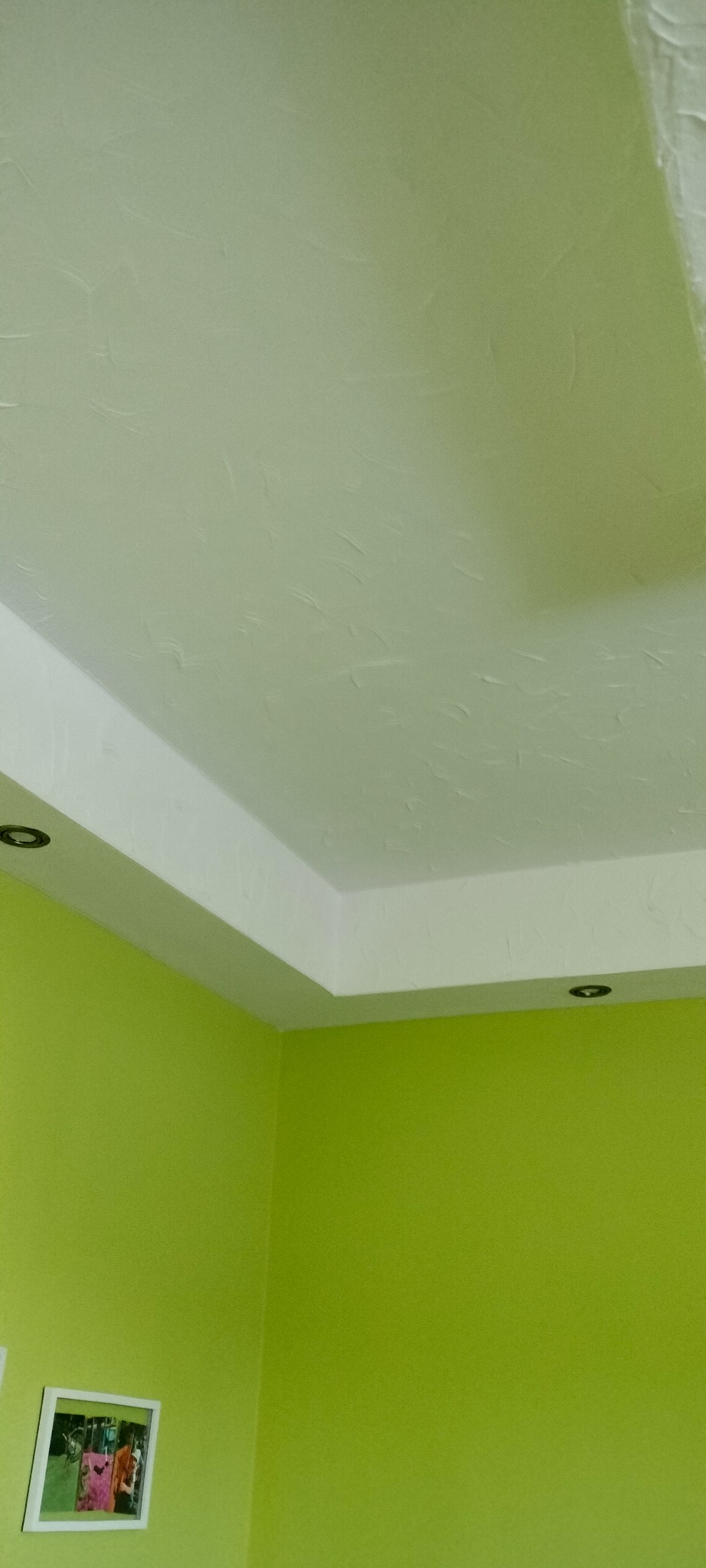 Ściana pomalowana na zielono z białym sufitem i listwą. Widoczny fragment obrazu w ramce. Teksturowana powierzchnia sufitu. Oświetlenie punktowe.
