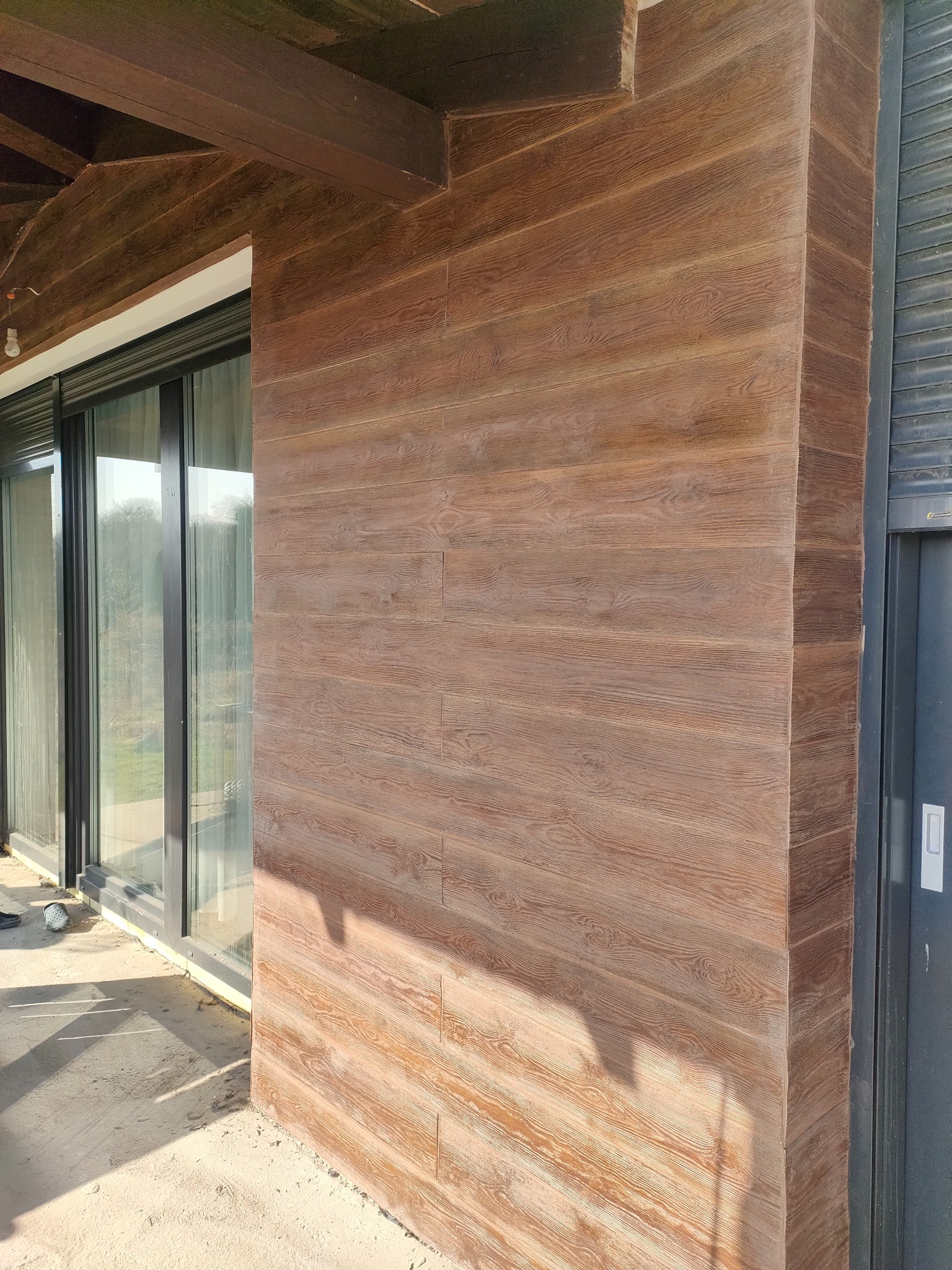 Elewacja budynku w Gniezno z drewnopodobną okładziną, widoczne przesuwne okna i fragment drzwi. Detal wykończenia zewnętrznego.