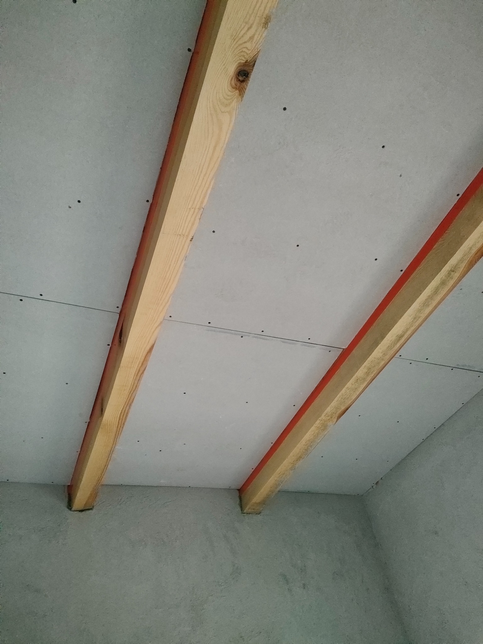 Montaż płyt karton gips na drewnianej konstrukcji sufitu. Widoczne łączenia płyt i mocowania. Surowy stan wykończenia wnętrza.