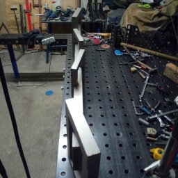 Tani-Spaw - Metalowe ramy na perforowanym stole spawalniczym, narzędzia w tle. Widoczne elementy konstrukcyjne w trakcie tworzenia, warsztatowy nieład.