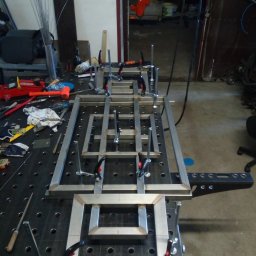 Tani-Spaw - Spawanie konstrukcji metalowej z profili zamkniętych na stole spawalniczym. Elementy mocowane ściskami stolarskimi. Widoczne narzędzia i materiały spawalnicze.