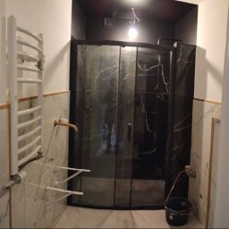 KRISTALGRESBUD VLADYSLAV BERNATSKYI - Częściowo wykończona łazienka w Zielonej Górze: kabina prysznicowa z czarnymi płytkami imitującymi marmur, grzejnik drabinkowy i marmurowe płytki ścienne.