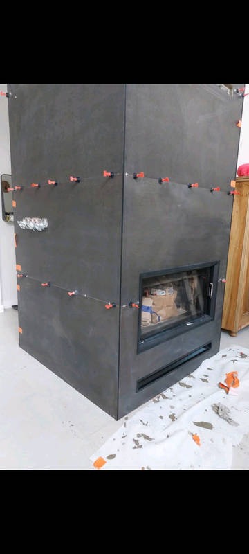 Obudowa kominka z szarych płyt, w trakcie montażu, z widocznymi krzyżykami dystansowymi. Na podłodze folia ochronna z zabrudzeniami.