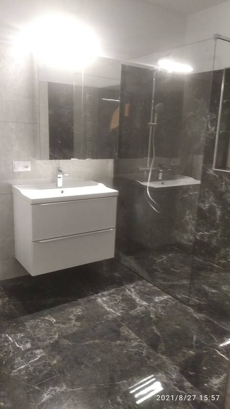 Nowoczesna łazienka z marmurową podłogą i ścianami, białą szafką pod umywalką i szklaną kabiną prysznicową. Minimalistyczny design, jasne oświetlenie.