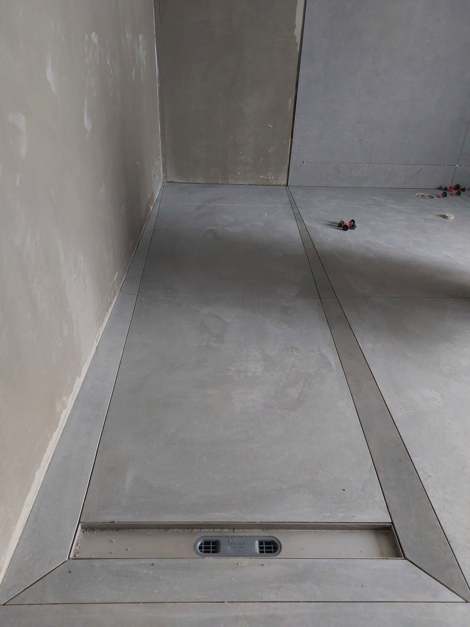 Ułożona szara podłoga z odpływem liniowym w łazience w Zielonej Górze. Widoczne płytki i fugi. Ściany przygotowane do dalszych prac wykończeniowych.