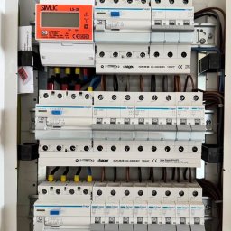 Nobisend - Rozdzielnica elektryczna z zabezpieczeniami Hager, widoczne przewody z oznaczeniami kolorystycznymi i licznik energii Simlic LS-3F. Estetyczne i uporządkowane ułożenie.