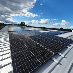 Nobisend - Rząd paneli słonecznych na metalowym dachu w słoneczny dzień z chmurami. Widok z góry, instalacja fotowoltaiczna na dachu budynku.