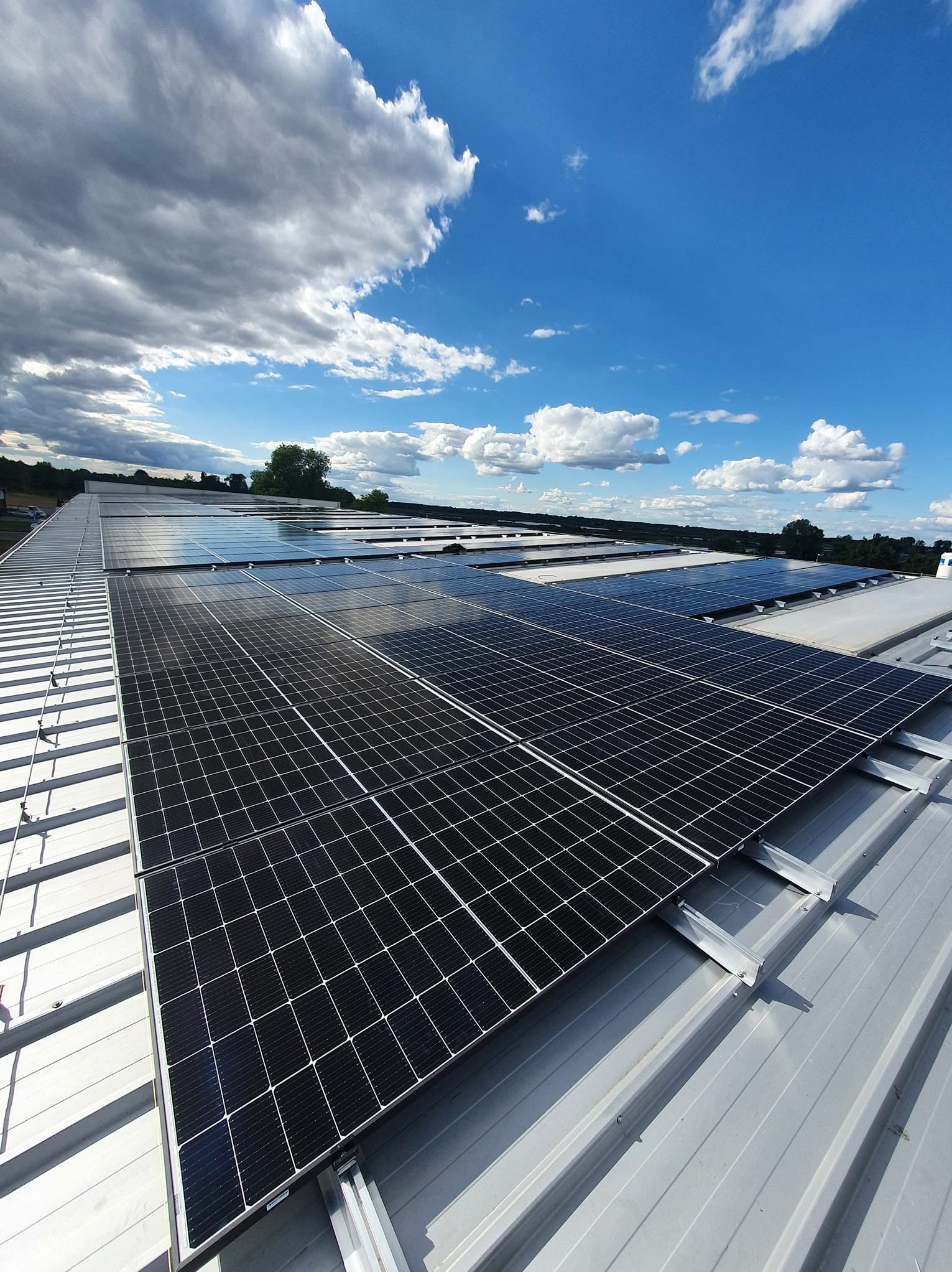 Rząd paneli słonecznych na metalowym dachu w słoneczny dzień z chmurami. Widok z góry, instalacja fotowoltaiczna na dachu budynku.