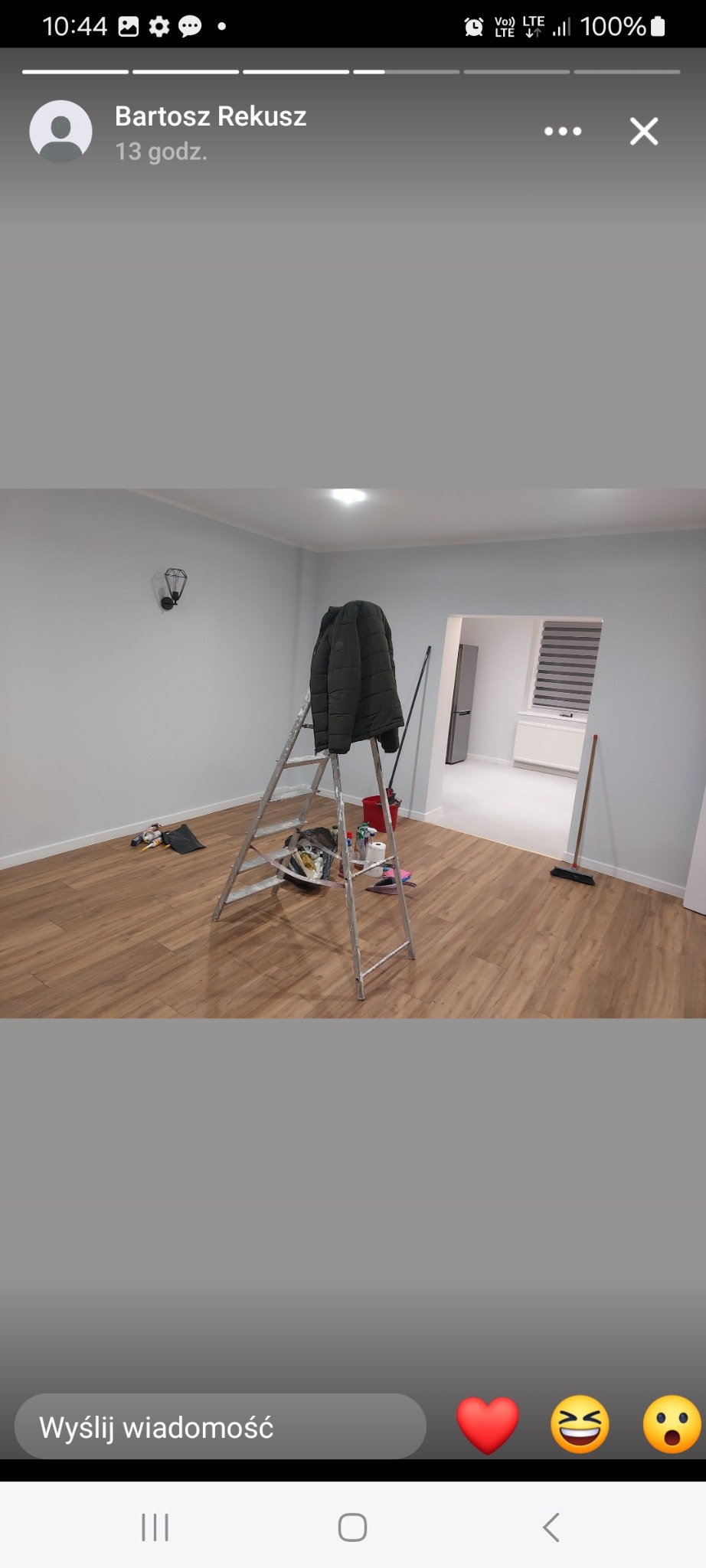 Wnętrze po malowaniu: jasne ściany, drewniana podłoga, drabina z kurtką, widok na sąsiednie pomieszczenie. Świeżo odmalowane mieszkanie.