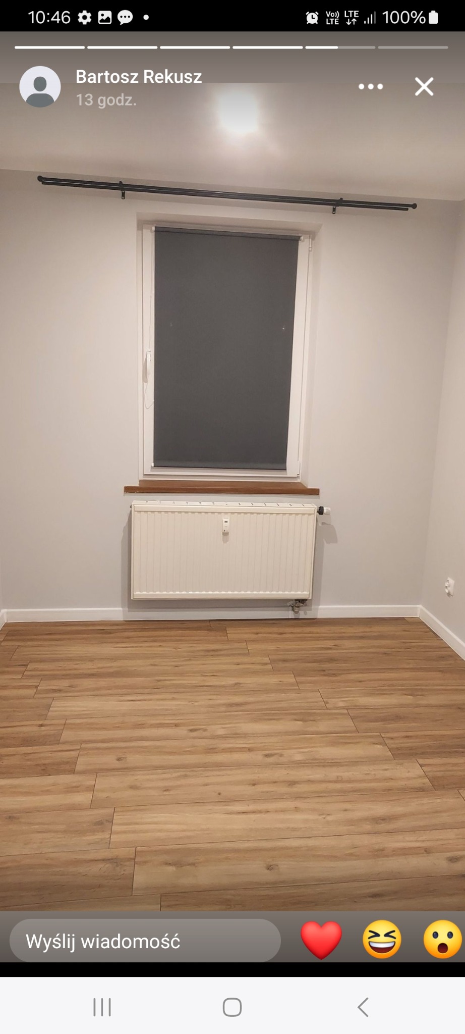 Jasne wnętrze pokoju po malowaniu: białe ściany, drewniana podłoga, okno z roletą i grzejnik. Minimalistyczny wystrój, świeżo po remoncie.