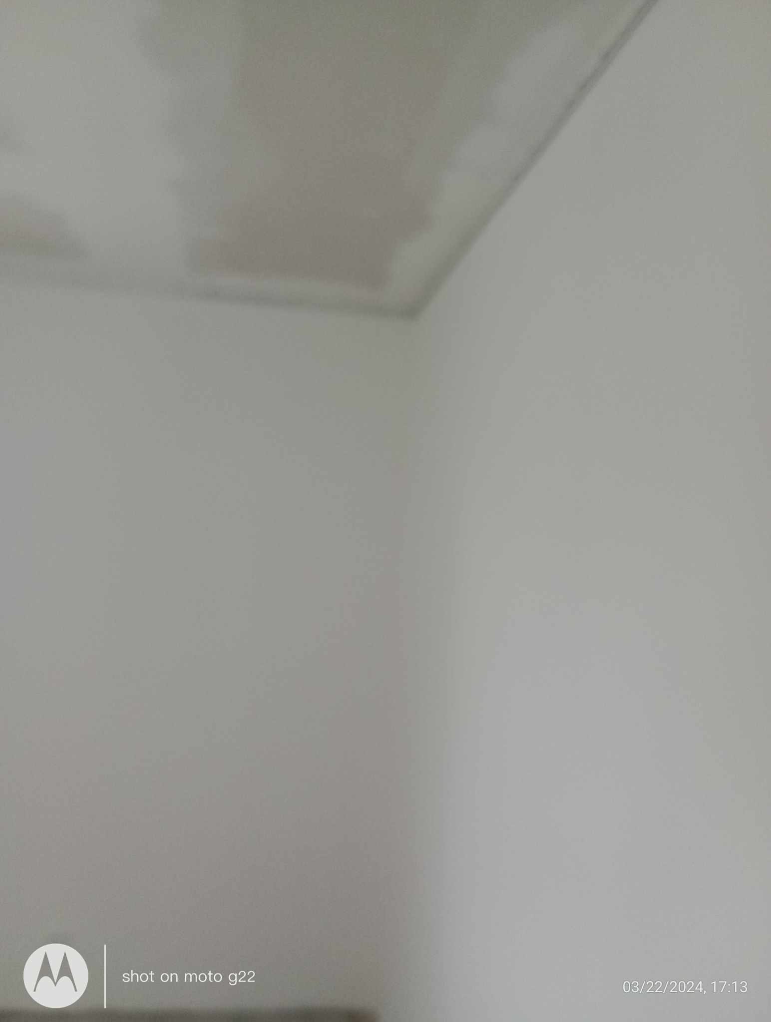 Świeżo pomalowany, jasnoszary sufit w rogu pokoju, widoczne delikatne smugi farby. Minimalistyczne wnętrze, neutralna kolorystyka.