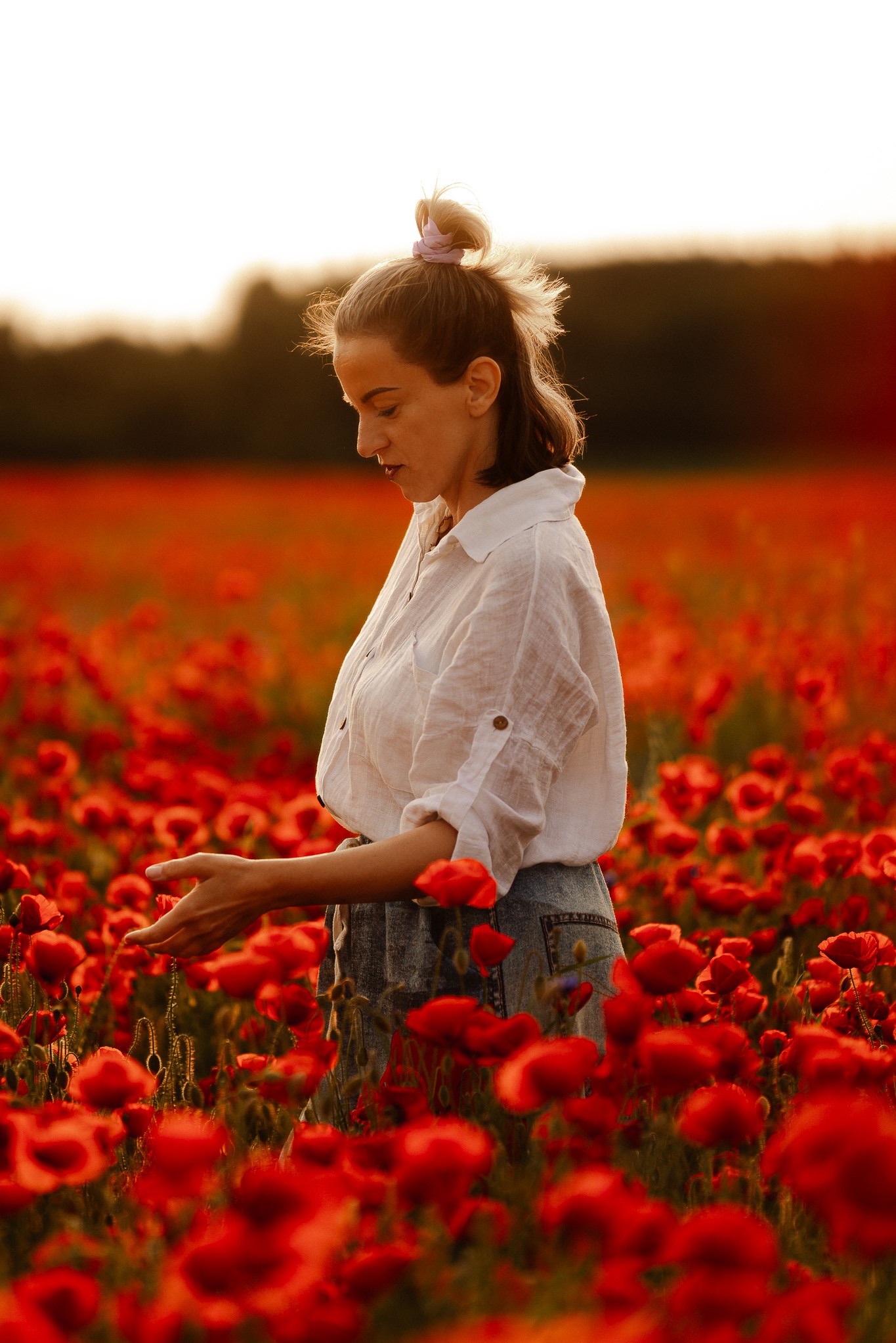 Kobieta w białej koszuli na tle pola maków w ciepłym, zachodzącym słońcu. Profil, delikatne światło, naturalna sceneria. Romantyczna atmosfera.