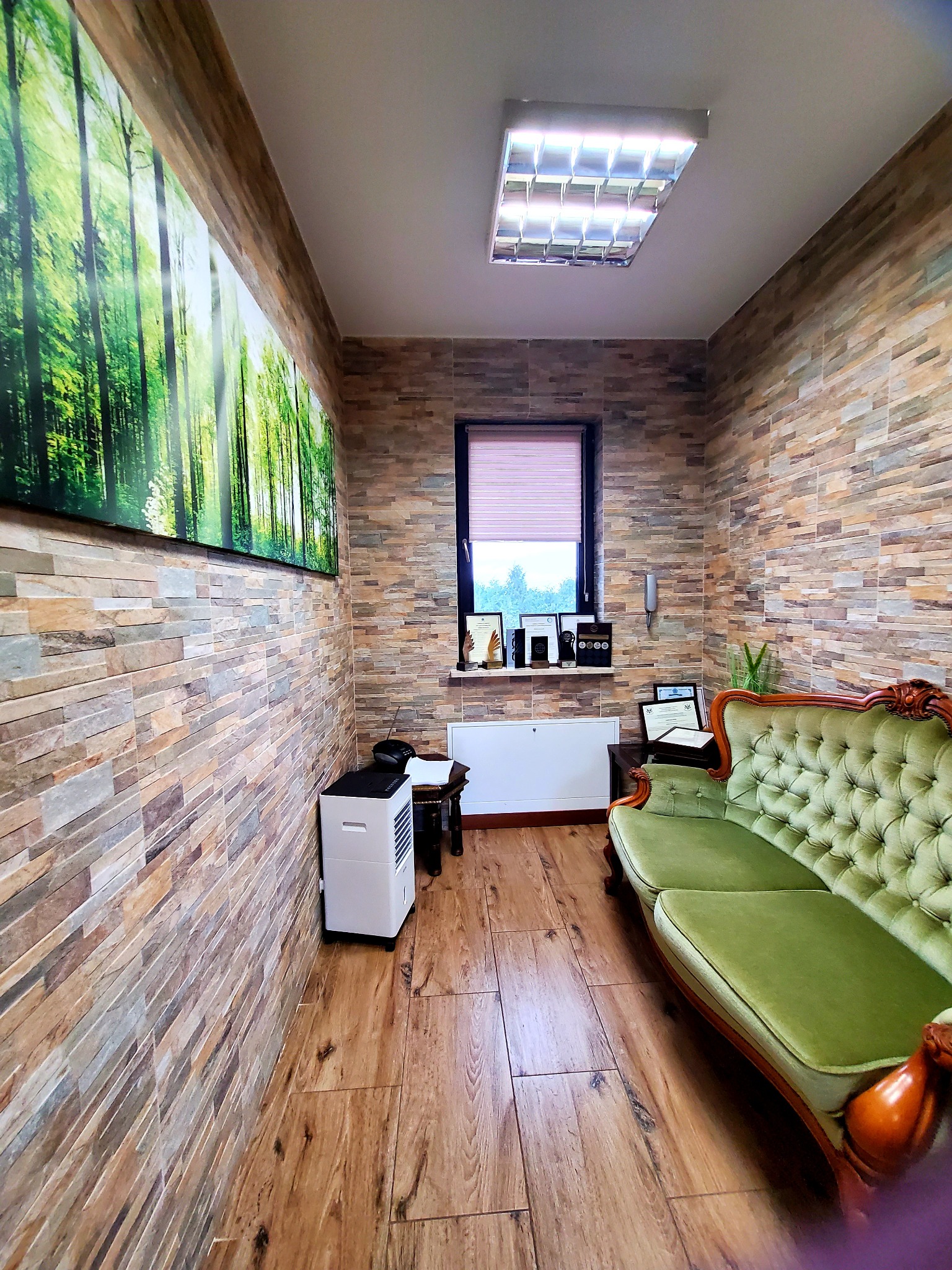 Gabinet z zieloną sofą Chesterfield, ścianami z kamienia dekoracyjnego i obrazem lasu. Przytulne wnętrze z elementami vintage i nowoczesnymi.