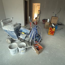 F.H.U AGNIESZKA STANIKOWSKA - Wnętrze w trakcie prac wykończeniowych: ściany przygotowane do malowania, widoczny agregat malarski, wiadra z farbą i narzędzia. Przygotowanie do malowania natryskowego.