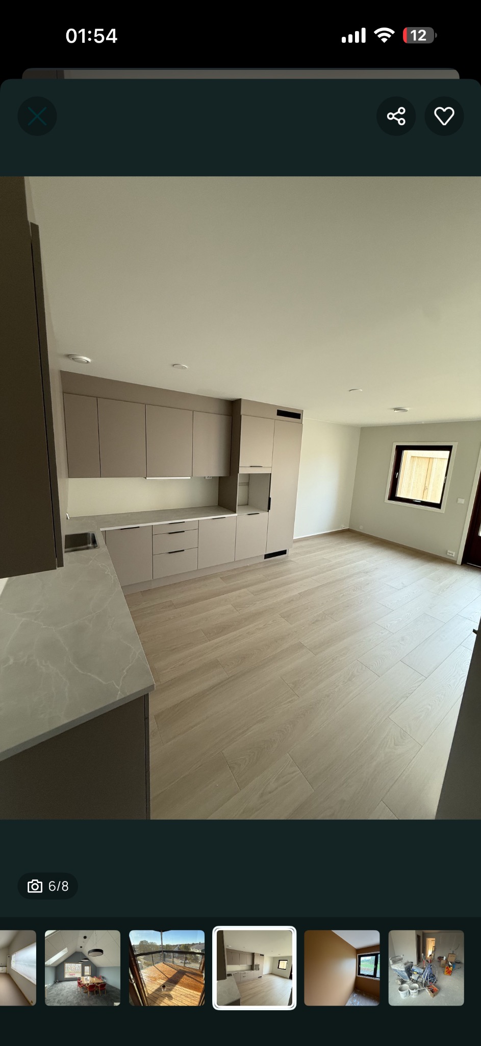 Jasna kuchnia z beżowymi szafkami i drewnopodobną podłogą. Widoczne okno i fragment blatu. Minimalistyczny styl wykończenia wnętrza.