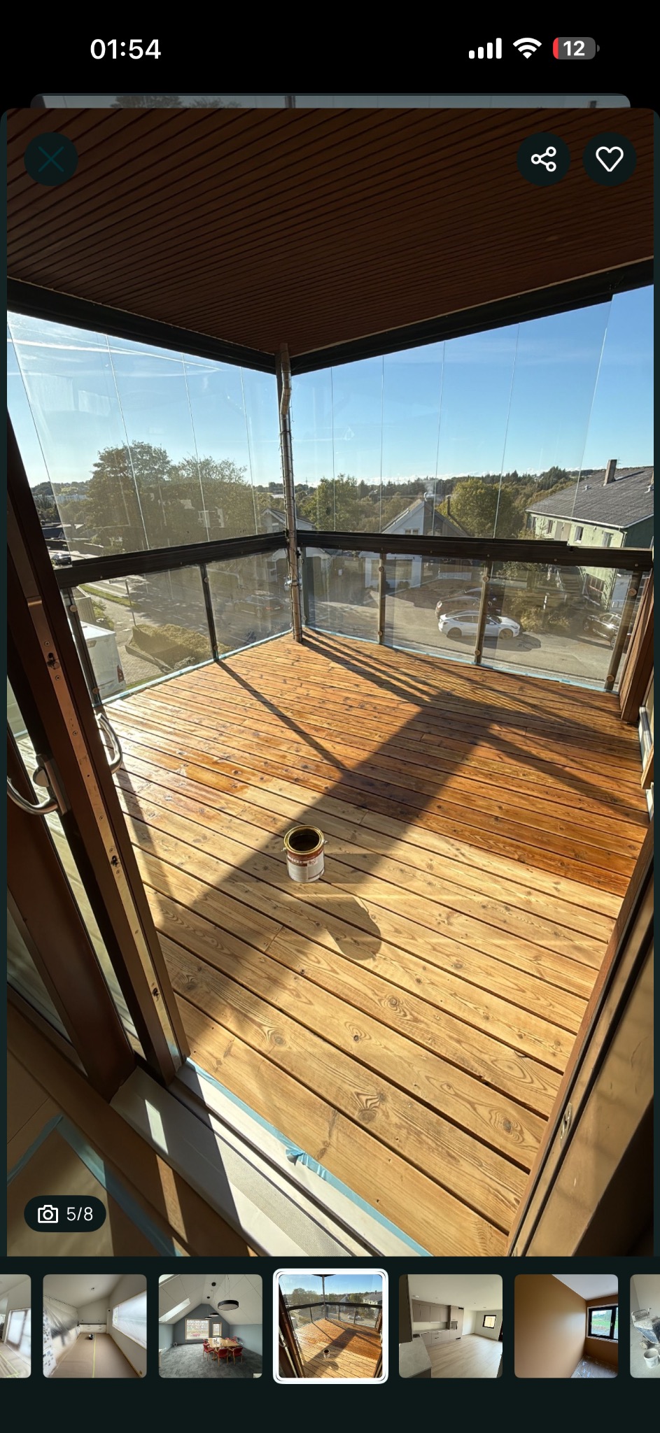 Drewniany balkon z przeszklonymi ścianami po malowaniu. Widoczna puszka z farbą i świeżo pomalowana podłoga z desek. Słoneczny dzień.