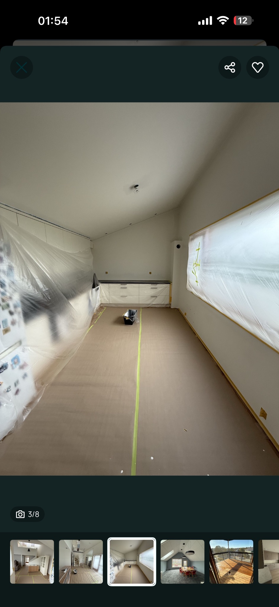 Przygotowane do malowania wnętrze: zabezpieczone folią okna i meble, podłoga wyłożona kartonem z taśmą malarską. Widoczny pojemnik na farbę.