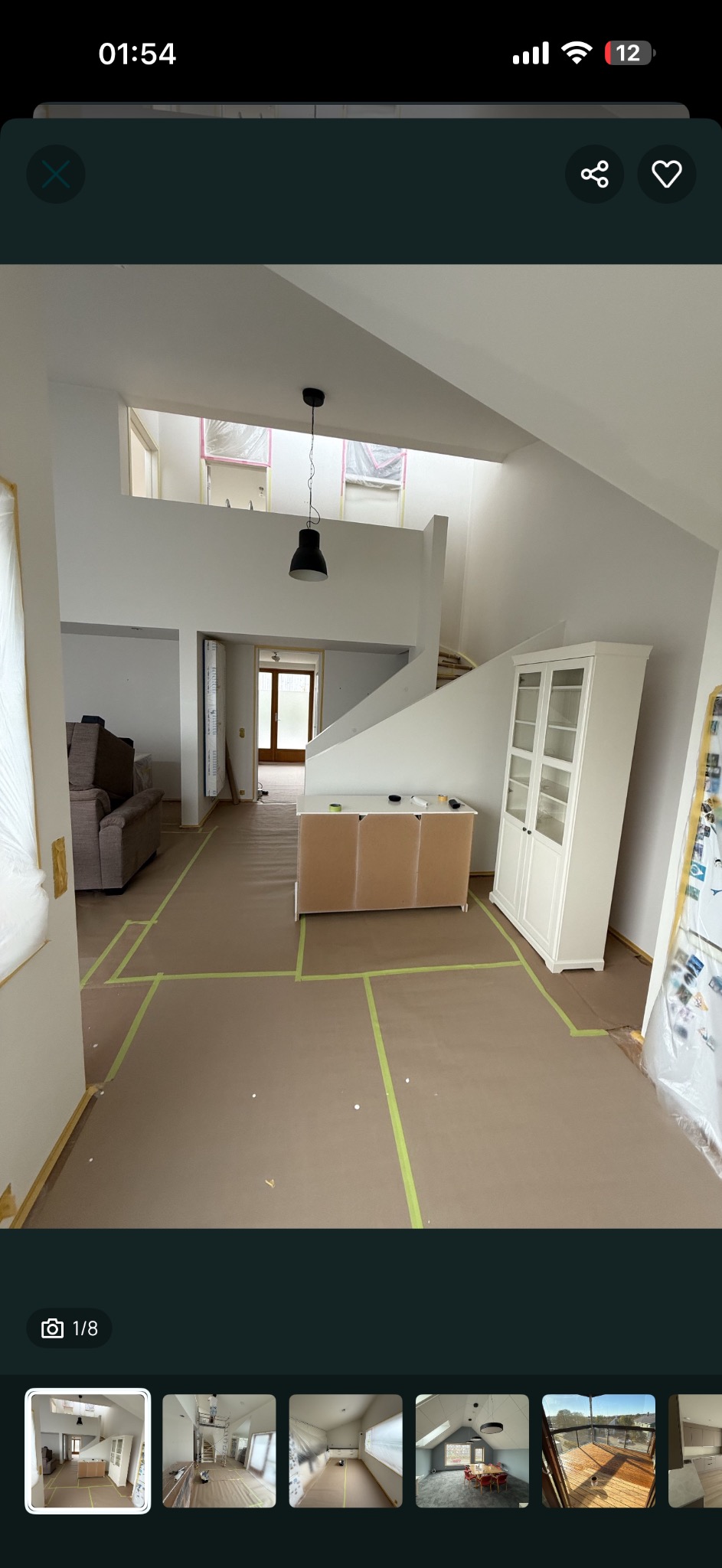 Przygotowane do malowania wnętrze domu z zabezpieczonymi podłogami i meblami. Widoczne wysokie ściany, schody i okna dachowe. Oświetlenie: czarna lampa.