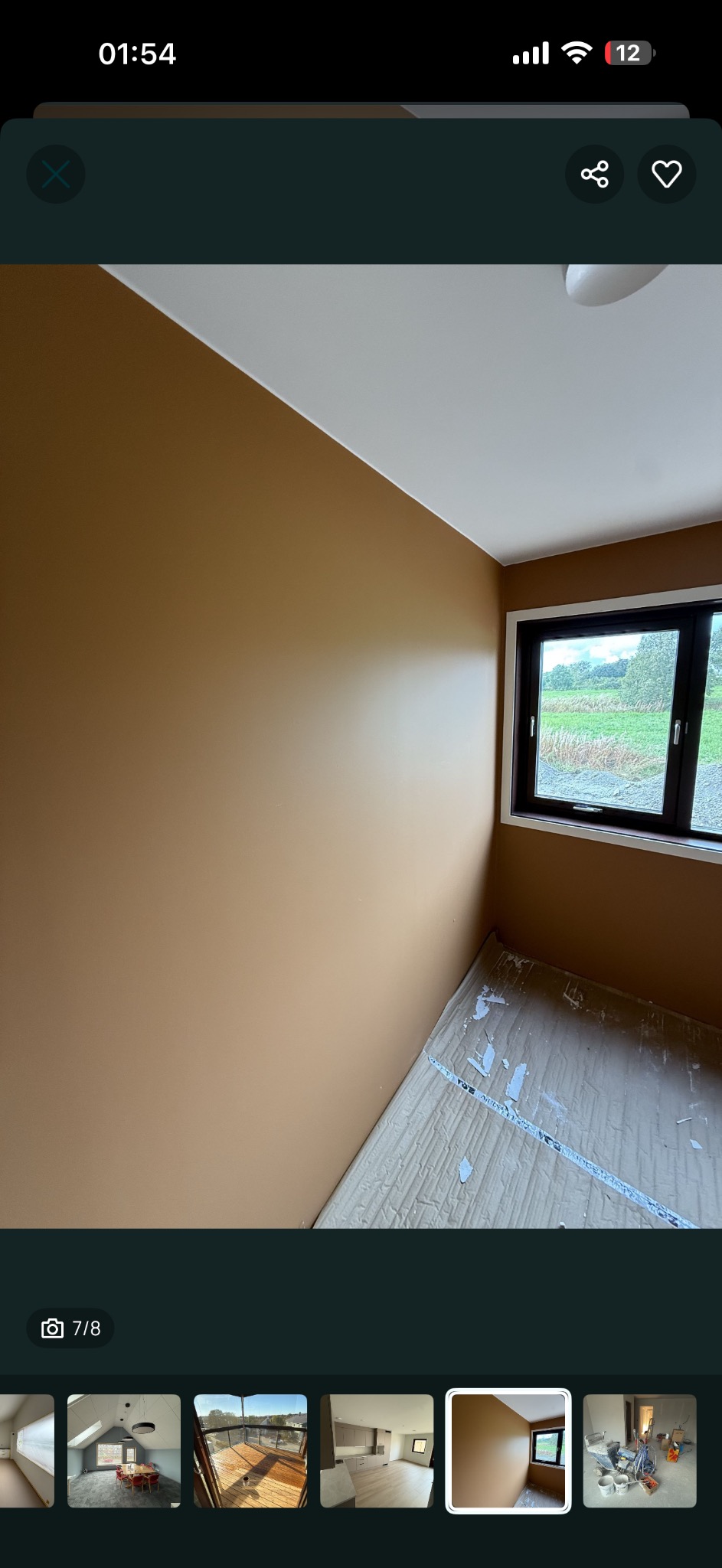 Ściana w odcieniach brązu po malowaniu, widok na okno z widokiem na zieleń. Podłoga zabezpieczona kartonem. Świeżo pomalowane wnętrze.