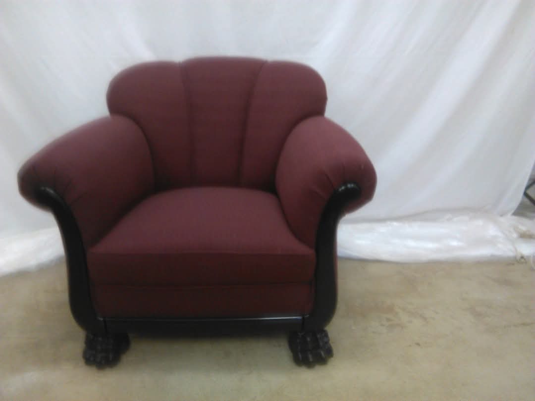 Burgundowy fotel klubowy z ciemnym drewnianym wykończeniem i dekoracyjnymi nóżkami na tle białej tkaniny. Widok z przodu, oświetlenie studyjne.