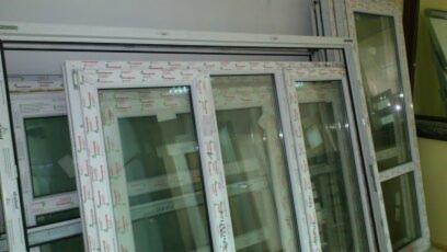 Stos białych, nie zamontowanych ram okiennych z szybami, widoczne profile z nadrukowanym wzorem, ustawione obok siebie.