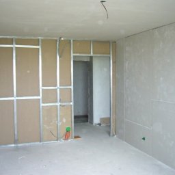 CRAFT Oleksandr Karpenko - Montaż ścian działowych z płyt karton-gips na metalowym stelażu w surowym wnętrzu. Widoczne przewody elektryczne i otwór drzwiowy.