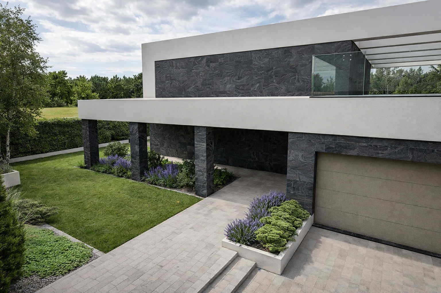 Nowoczesny dom z garażem, kamienną elewacją i zadbanym ogrodem z równo przystrzyżonym trawnikiem oraz rabatami z lawendy i krzewów.