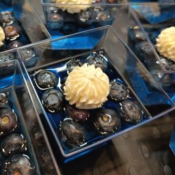 FoodArt Grzegorz Roman - Deser w przezroczystym pojemniku: borówki w niebieskiej galaretce, zwieńczone kremem. Widok z góry, ostre światło podkreśla detale.