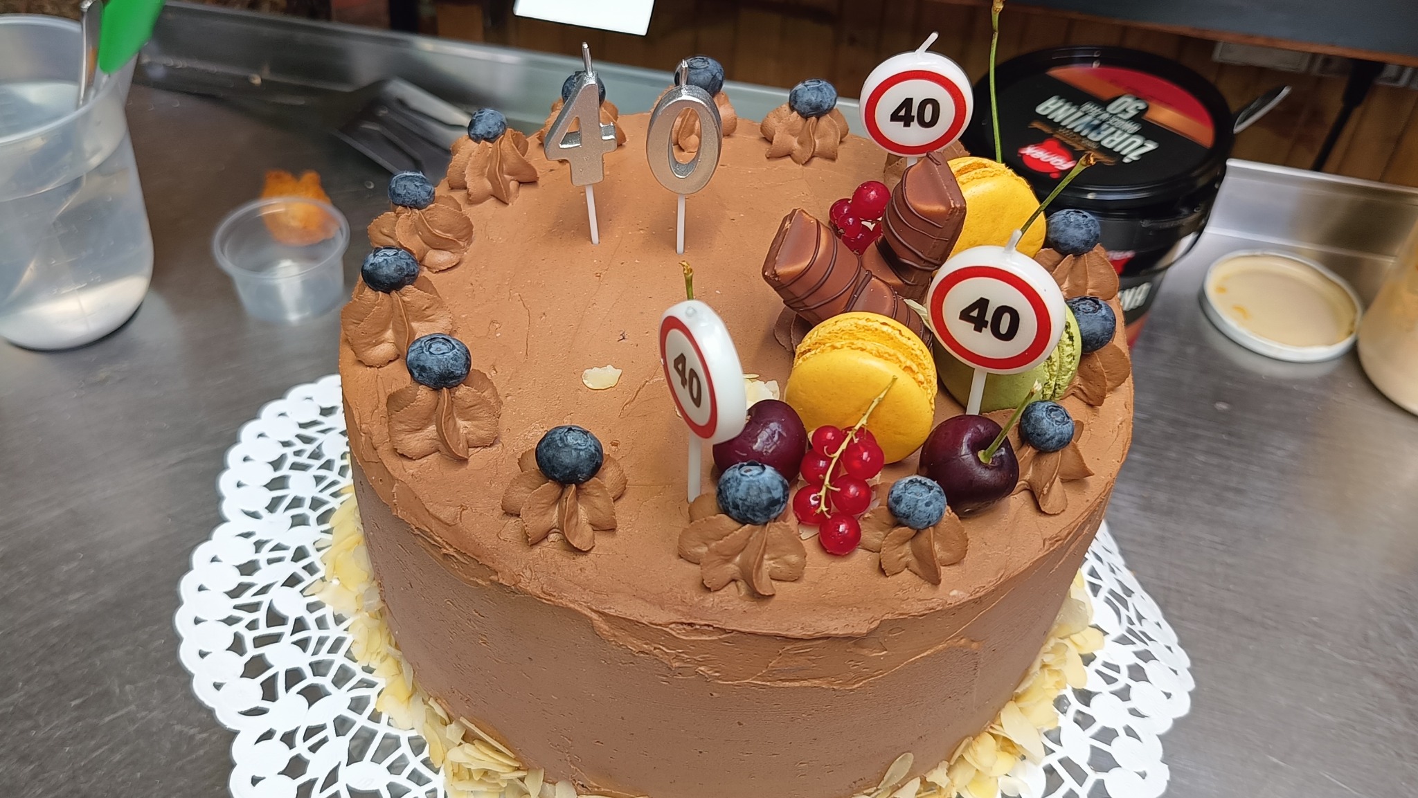 Tort czekoladowy na 40 urodziny, udekorowany borówkami, wisienkami, makaronikami i świeczkami w kształcie znaków drogowych '40'.