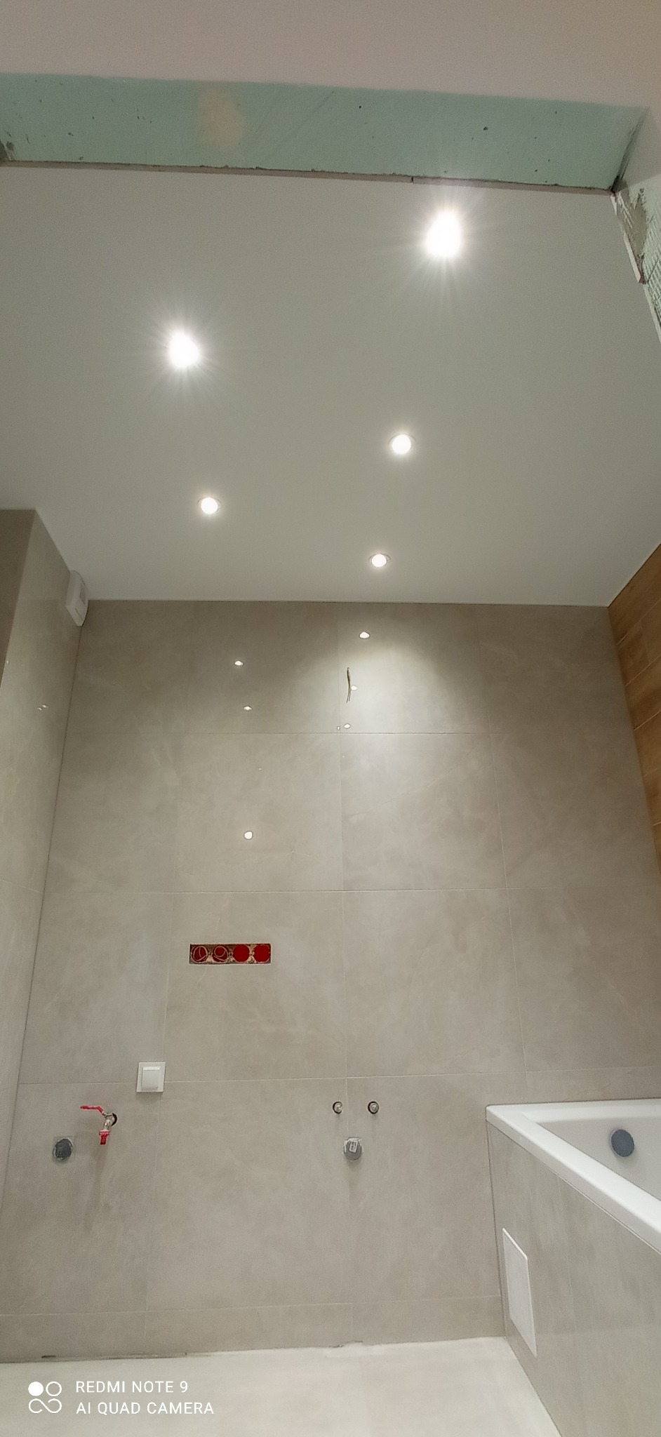 Jasna łazienka po remoncie z zamontowanym oświetleniem punktowym, płytkami w odcieniach beżu i przygotowanymi przyłączami wodno-kanalizacyjnymi.