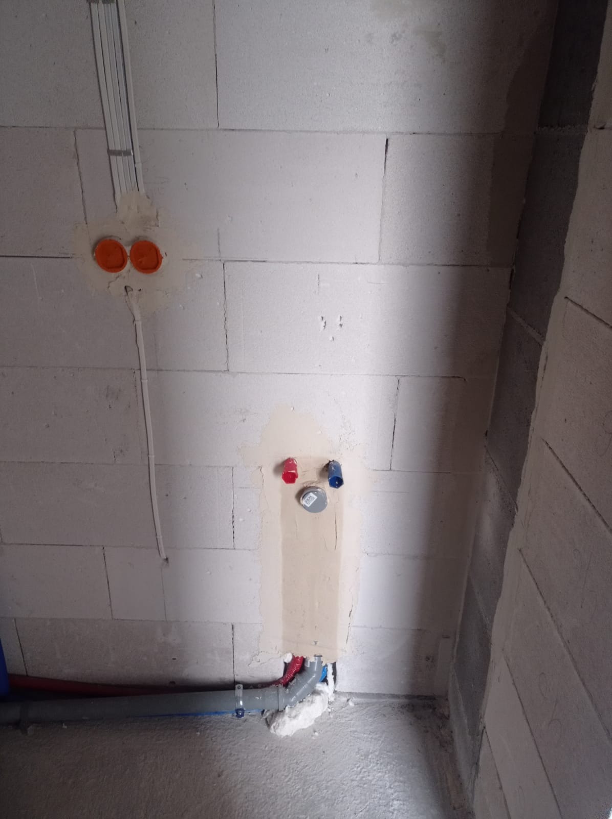 Instalacja wodno-kanalizacyjna w surowym wnętrzu: rury, puszki elektryczne i otwory w ścianie z betonu komórkowego, przygotowane do dalszych prac wykończeniowych.