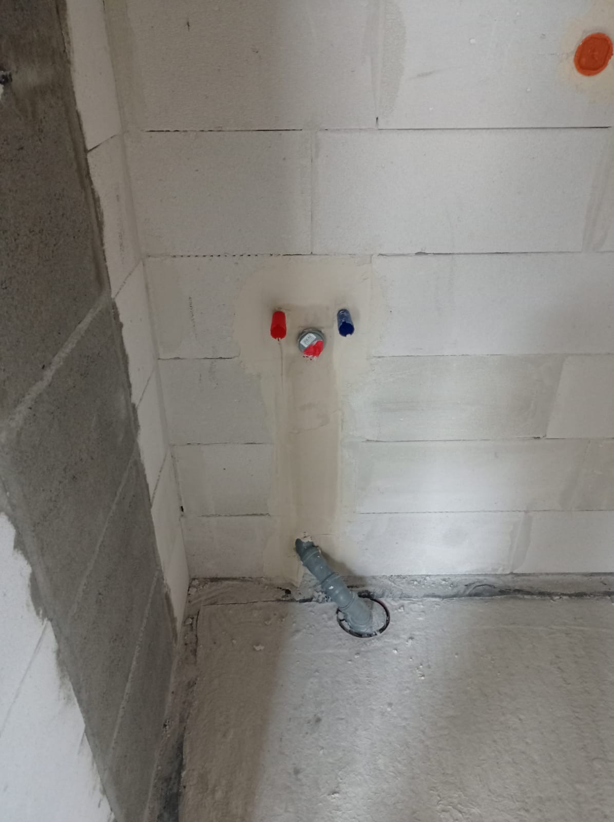 Ściana z betonu komórkowego z wyprowadzonymi rurami instalacji wodnej (czerwona, niebieska) i kanalizacyjnej. Widoczne ślady po zaprawie.