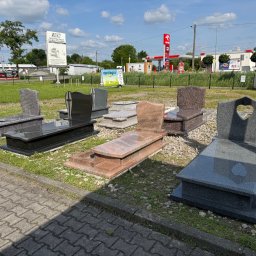Kamieniarstwo Sati - Wystawa nagrobków z granitu i marmuru w różnych kolorach i wzorach, ustawionych na trawie przed kamieniarstwem. W tle stacja benzynowa Orlen.