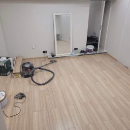 REMONTOVNIA Bartłomiej Wieciński - Jasne panele podłogowe ułożone w pokoju z lustrem i otwartą garderobą. Widoczny odkurzacz i narzędzia, sugerujące prace wykończeniowe w trakcie realizacji.