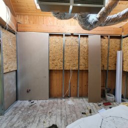 Hubert Słaboń - Wnętrze w trakcie remontu: metalowa konstrukcja, płyty OSB, częściowo zamontowane płyty karton-gips, widoczne instalacje i plany na podłodze. Drewniany strop z wentylacją.