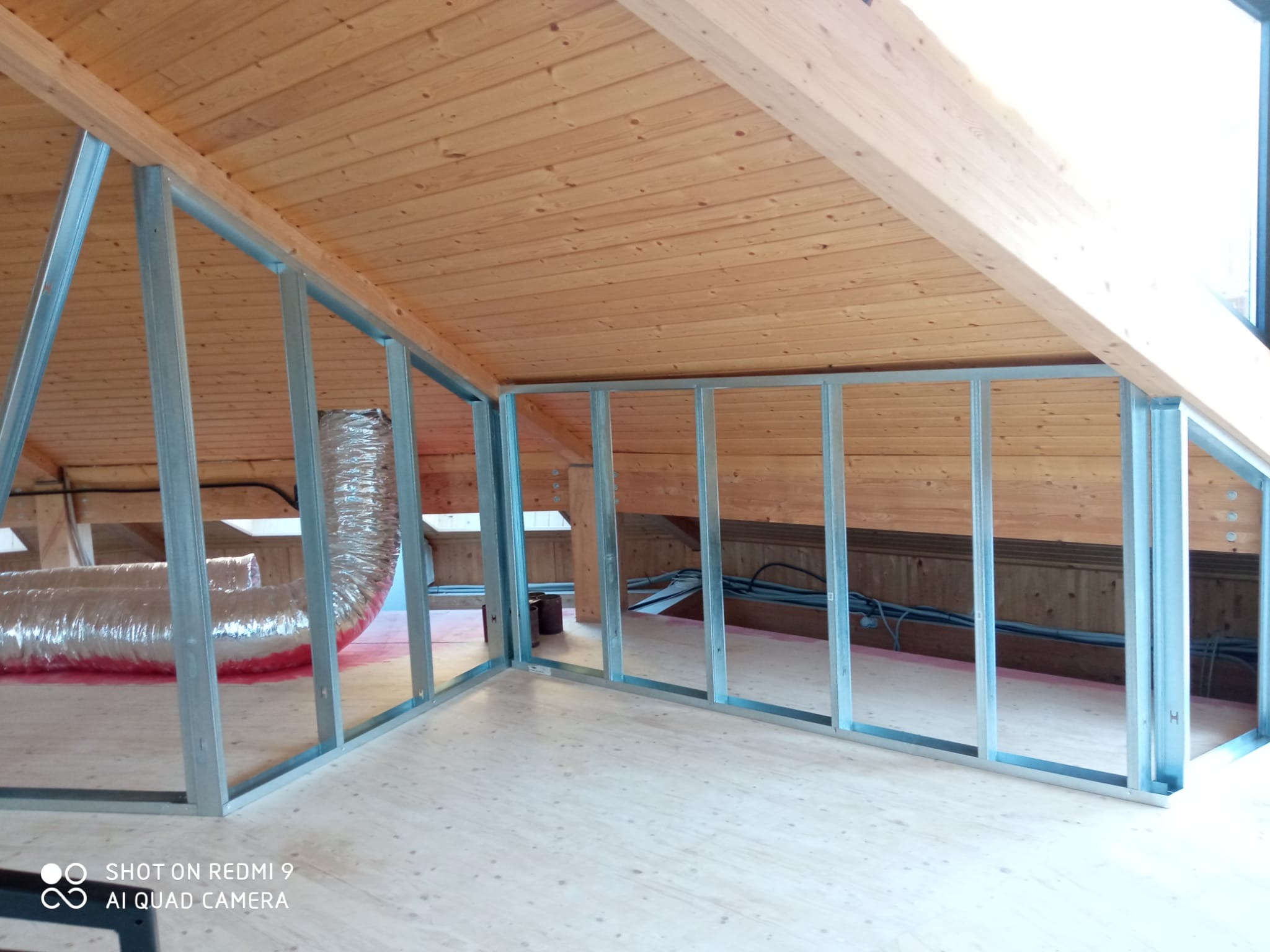 Stelaż z profili metalowych w surowym wnętrzu poddasza z drewnianą boazerią, widoczne przewody wentylacyjne i instalacje. Przygotowanie do wykończenia.