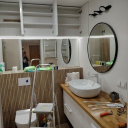 STABART - Montaż szafek i umywalki w łazience z drewnianymi panelami. Widoczna drabina i narzędzia. Realizacja z Gniezna. Nowoczesny styl.