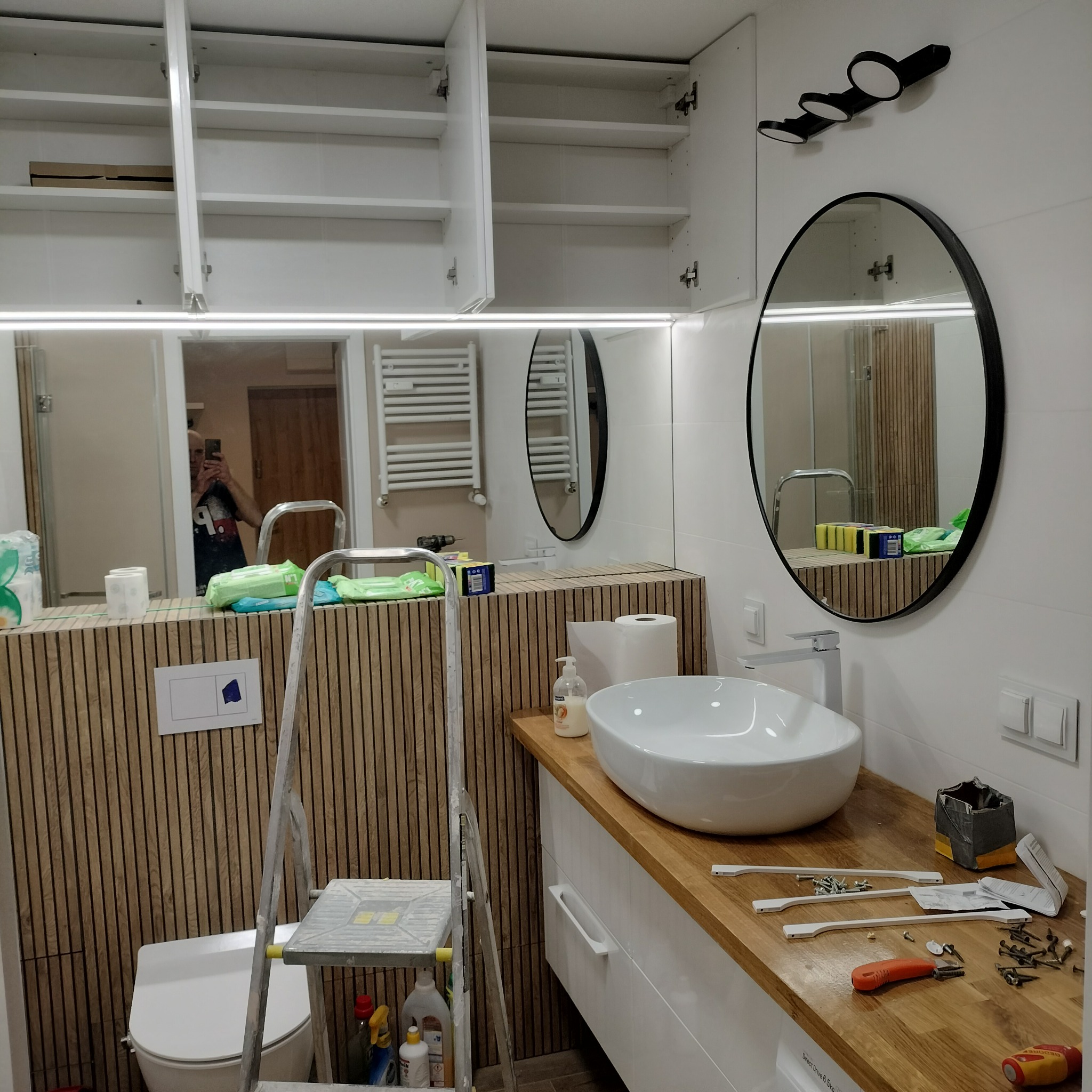 Montaż szafek i umywalki w łazience z drewnianymi panelami. Widoczna drabina i narzędzia. Realizacja z Gniezna. Nowoczesny styl.