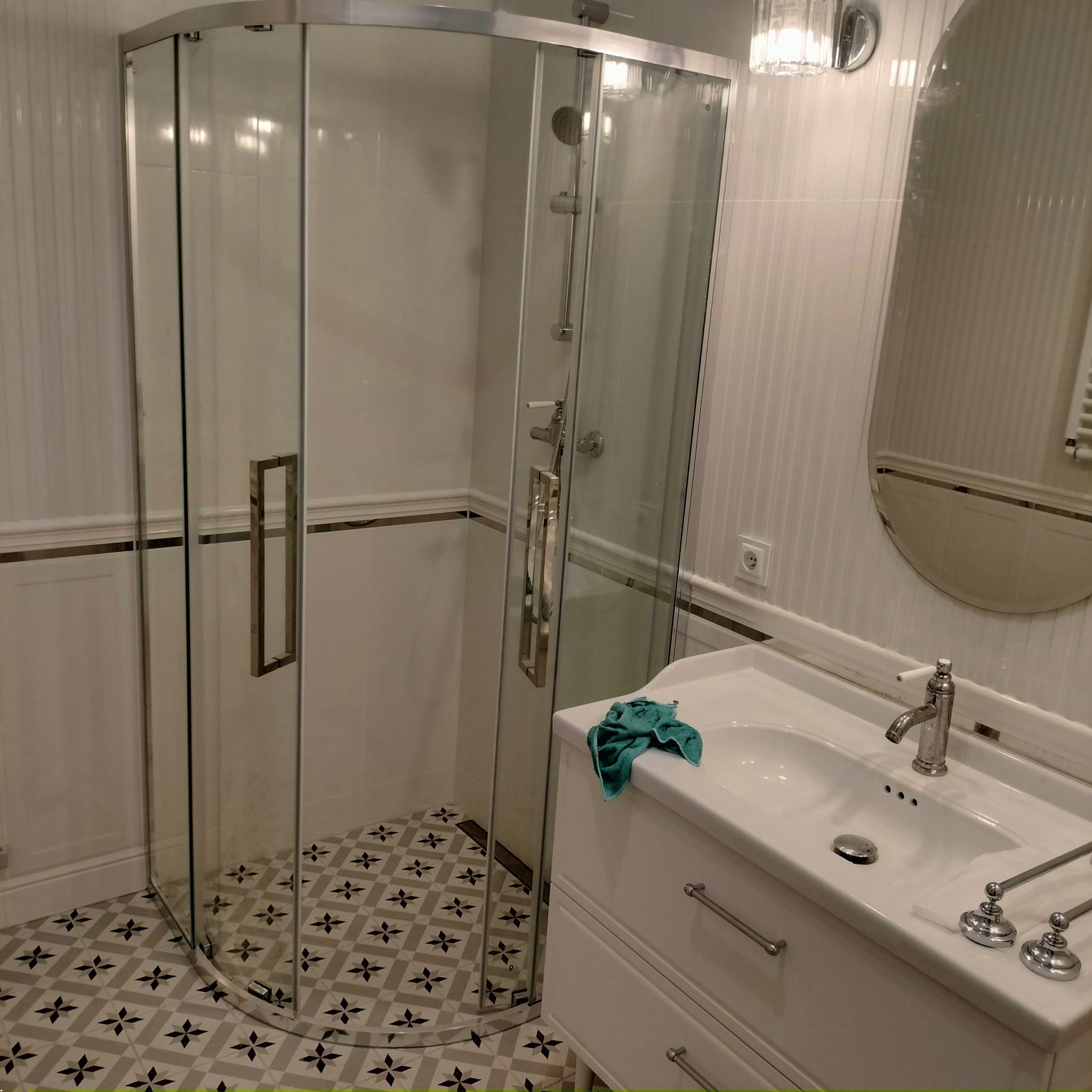 Wykończona łazienka: kabina prysznicowa narożna, biała umywalka z szafką, wzorzysta podłoga. Nowoczesny design z elementami klasycznymi.