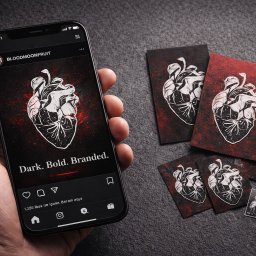 Shinedesing Klaudia Pikulik - Telefon w dłoni prezentuje post z grafiką serca na Instagramie BLOODMOONFRUIT, obok leżą wizytówki z tym samym motywem na ciemnym tle z czerwonymi akcentami.