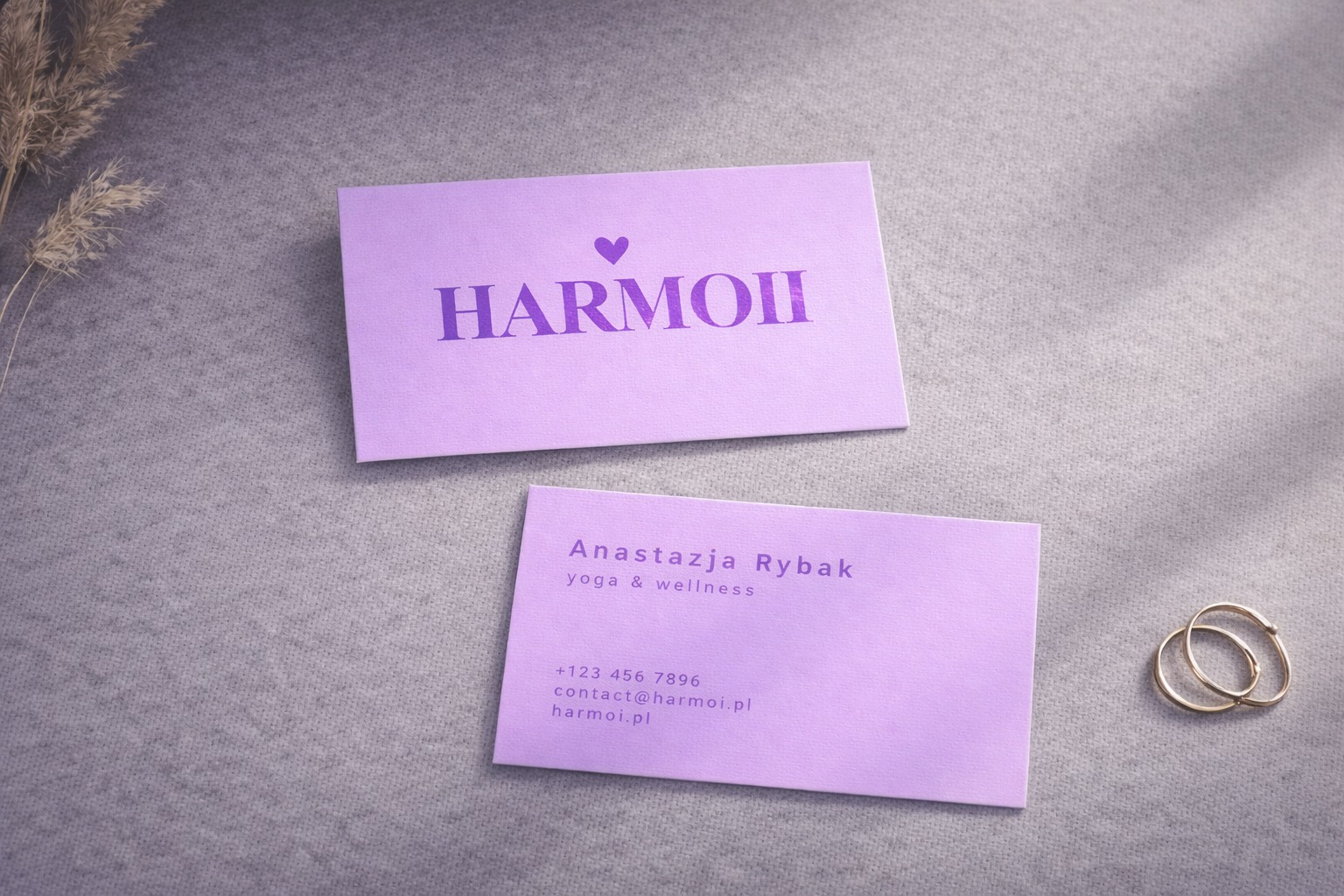 Dwie fioletowe wizytówki na szarym tle z gałązką i pierścionkami. Górna wizytówka z napisem HARMOII i sercem, dolna z danymi kontaktowymi Anastazji Rybak.