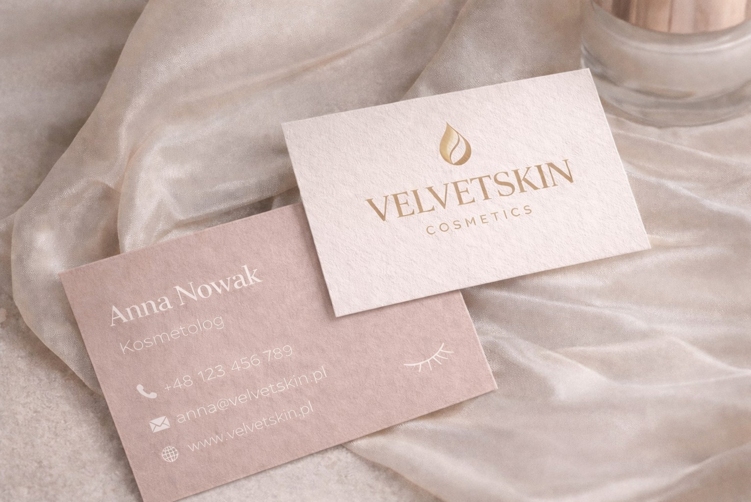 Dwie wizytówki na jedwabnej tkaninie: jedna z logo 'VelvetSkin Cosmetics', druga z danymi kontaktowymi Anny Nowak, kosmetolog. Subtelna kolorystyka, minimalistyczny design.