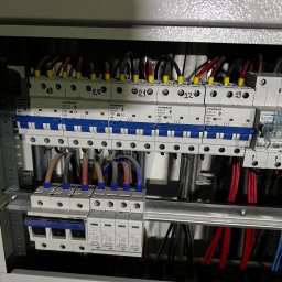 MultiSystem - Rozdzielnica elektryczna z bezpiecznikami i przewodami oznaczonymi numerami, widoczne elementy instalacji elektrycznej wewnątrz szafy.
