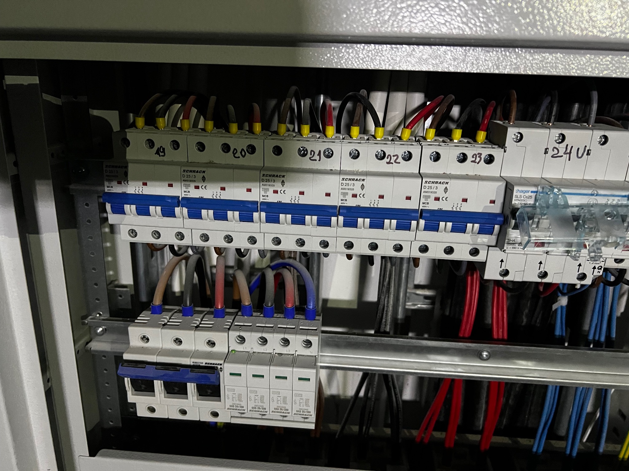 Rozdzielnica elektryczna z bezpiecznikami i przewodami oznaczonymi numerami, widoczne elementy instalacji elektrycznej wewnątrz szafy.