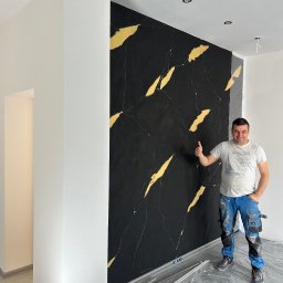 ADIKRISBAU Remonty i Wykończenia Krzysztof Smaza - Ściana z efektem czarnego marmuru i złotych żył, wykonana przez uśmiechniętego fachowca w roboczym stroju, z uniesionym kciukiem w górę. Podłoga zabezpieczona folią.