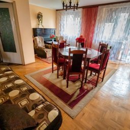 Monika Rakowska Usługi - Salon z pianinem, stołem i krzesłami w stylu vintage, dywanem z motywem kwiatowym i parkietem. Widok na okno z firankami i telewizor na komodzie.