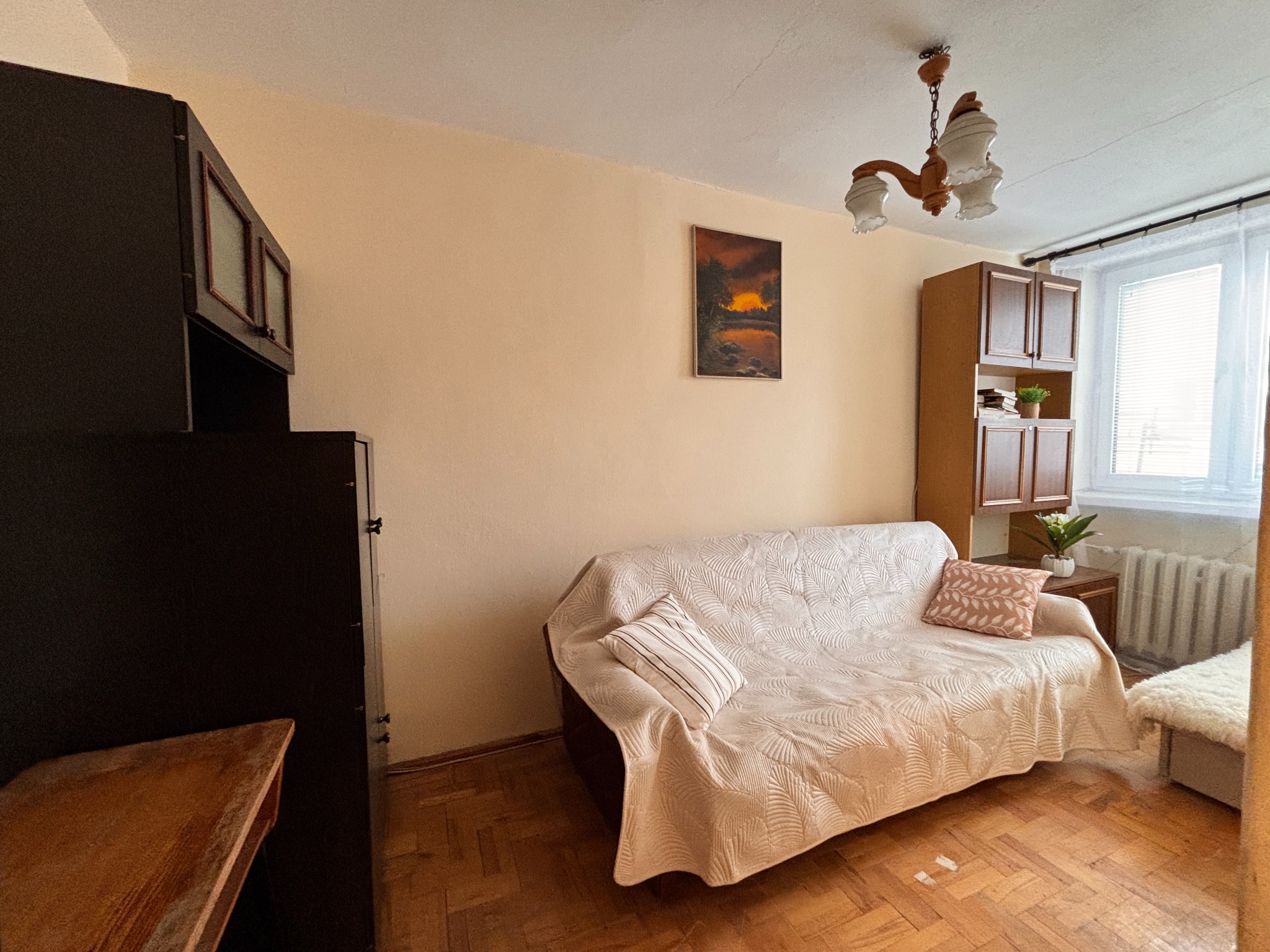 Jasne wnętrze pokoju po home stagingu: sofa z narzutą w liście, obraz na ścianie, drewniana podłoga i meble. Przytulna aranżacja z elementami dekoracyjnymi.